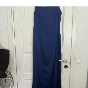 Marinblå långklänning från Nelly - Säljer en stilren marinblå långklänning från Nelly i slät polyester. Klänningen har en figurnära passform, är ärmlös och har en snygg dragkedja i sidan. Perfekt för dig som vill ha en enkel men elegant look med lite edge.