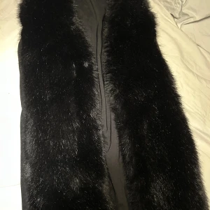 Svart pälsväst från Michael Kors - Snygg svart pälsväst från Michael Kors i storlek S. Västen har breda pälsdetaljer framtill och är helsvart med slät baksida. Perfekt för att addera lite lyx till din outfit. Fodrad insida för extra komfort och stil.