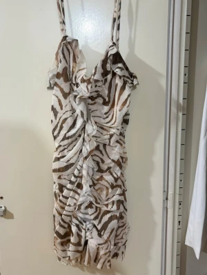 Zebramönstrad kort klänning med volanger - Supersnygg kort klänning med zebramönster i vitt och brunt. Klänningen har smala axelband, volangdetaljer framtill och en figurnära passform.✨