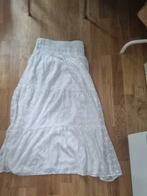 Vit långkjol med volang och mönster - Säljer en vit långkjol med. Kjolen har volangdetaljer och är gjord i ett lätt material som passar perfekt till varmadagar.