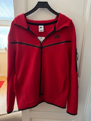 Röd Nike tech hoodie - Säljer denna feta röda Nike tech hoodie helt oanvänd i helt nytt skick!  Storleken L. Hör av er vid minsta lilla funderingar!✌️