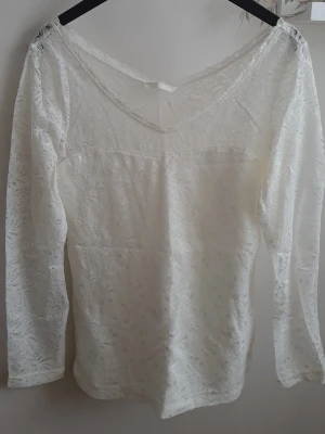 Vit spetsblus från H&M - Säljer en superfin vit vringad spetsblus från H&M. Toppen har ett detaljerat spetsmönster över hela tyget och är lätt transparent upptill. Den har diskret blänkande detaljer. Storleks lappen är bortklippt tyvärr.