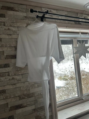 Vit omlottopp med knytband - Säljer en vit omlottopp med knytband i midjan. Toppen har en enkel design med rund hals och trekvartsärmar. Materialet är mjukt och känns som bomull, perfekt för dig som gillar stilrena och bekväma plagg. Passar dig som vill ha en fräsch och clean look.