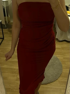 Röd bandeau klänning  - Säljer en snygg röd axelbandslös långklänning med tight passform. Klänningen har en slits bak och är figurnära med draperade detaljer på sidorna. Endast använd några gånger.