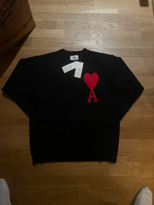 Svartets stickad tröja från Ami - Säljer en svart stickad tröja från Ami Alexandre Mattiussi med röd hjärtdetalj och bokstaven A på bröstet. Klassisk rund halsringning och långa ärmar. Perfekt för dig som vill ha en stilren men ändå unik look.
