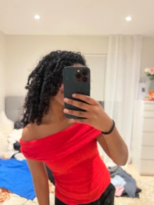 Röd offshoulder topp - Säljer en snygg röd offshoulder topp med bred krage som vilar över axlarna. Toppen är tight och har en ribbad struktur som ger en cool känsla. Perfekt att styla med jeans eller kjol för en trendig look.