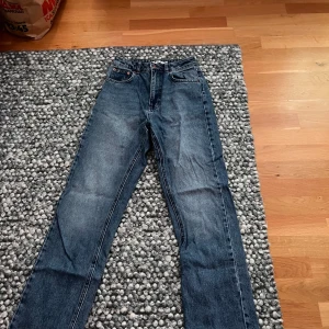 Blå raka jeans från NA-KD, stl 34 - Snygga blå jeans från NA-KD i rak modell med klassisk femficksdesign. Jeansen har hög midja och är tillverkade i ett robust denimtyg. Perfekta för dig som gillar en tidlös och clean look.