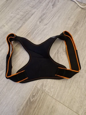 Hållningsstöd - Ett svart och oranget hållningsstöd som korrigerar en korrekt hållning för rygg och axlar. Köpt på Lidl för 130 kr för några år sedan men den är oanvänd. Använd gärna köp nu funktionen eller kom privat💗