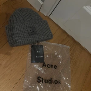  Acne Studios Mössa  - Säljer en grå ribbstickad mössa från Acne Studios med det ikoniska ansikts-emblemet framtill. Mössan är i mjukt material och har en bred uppvikt kant. 