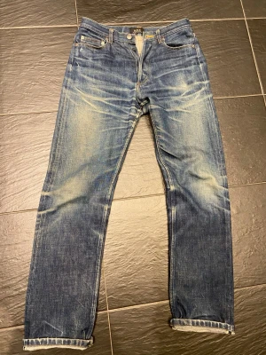 A.P.C. blå jeans med straight fit - Säljer ett par klassiska blå jeans från A.P.C. med snyggt slitna detaljer och raka ben. Jeansen har fem fickor, knappgylf och är tillverkade i robust denim. Perfekta för dig som gillar en tidlös och avslappnad look.