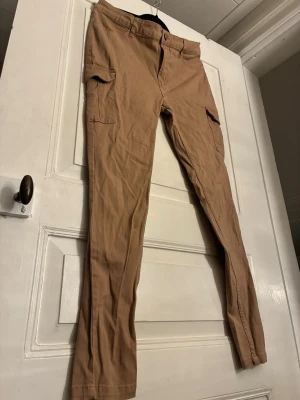 Beiga cargopants från 157, storlek M - Säljer ett par beiga cargopants från 157 i storlek M. Byxorna har raka ben, sidofickor med lock och bälteshällor. Tillverkade i mjuk bomull för skön känsla och avslappnad look. Perfekta för dig som gillar praktiska detaljer och enkel stil. Skulle säga att de passar S/M.