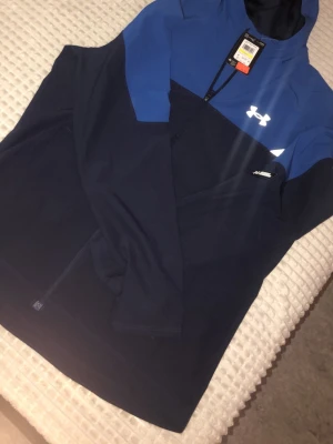 Blå och marinblå vindjacka Under Armour - Säljer en snygg vindjacka från Under Armour i blå och marinblå färg.  . Den är äkta med prislapp. Är aldrig använd. Kostar 1000 online eller i butik. Men jag säljer endast för 700.