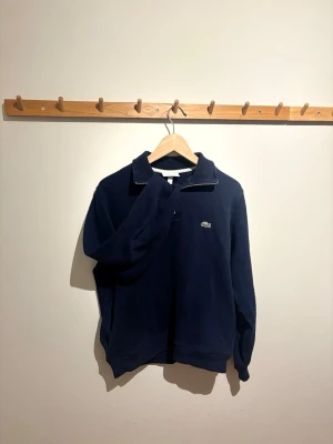Lacoste halv-zip  - Snygg och stilren Lacoste half zip i mörkblå (navy). Klassisk design med broderad krokodil på bröstet och praktiska sidofickor vilket är ovanligare på half zips och gör den extra nice.  Perfekt både till vardags och lite mer uppklätt. Mjuk och skön kvalitet, håller formen bra.😊 