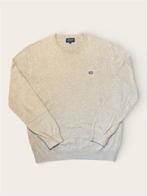 Beige stickad tröja från Lexington - Säljer en stilren beige stickad tröja från Lexington med rund halsringning och diskret logga på bröstet. Tröjan har ribbade muddar vid ärmslut och nederkant, perfekt för dig som gillar klassisk och enkel stil.