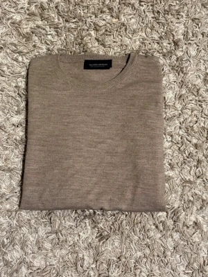  Stickad Tailored Originals - Säljer en stilren beige stickad tröja från Tailored Originals. Tröjan har rund halsringning och är i mjukt material som passar perfekt till lager på lager under höst och vinter. Enkel design som är lätt att matcha med olika outfits.