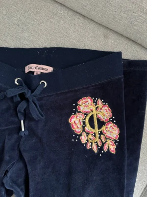 Juicy Couture mjukisbyxor - Ett par marinblå juicy couture mjukisbyxor. I ett mycket bra skick. Det är lågmidjade och har ett väldigt gulligt tryck på höften. Innerbens längd cirka 80cm. I storlek S men är mer åt xs hållet. 