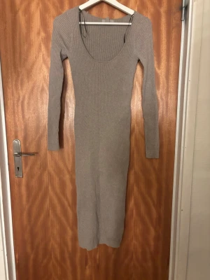 Beige ribbad stickad kläning  - Säljer en beige ribbad långklänning med lång ärm och rundad urringning. Klänningen är figurnära och har en stilren, enkel design som passar perfekt till många olika tillfällen. Klänningen är i en lite mörkare beige färg