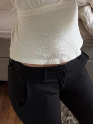 Svarta kostymbyxor med låg midija  - Säljer ett par svarta kostymbyxor med låg midja.Byxorna har bälteshällor, knapp och dragkedja framtill samt fickor på sidorna. 