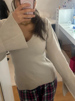 Beige stickad tröja med vida ärmar - Trendig beige stickad tröja med v-ringning och extra vida ärmar. Tröjan har ribbstickade muddar vid ärmslut och nederkant, vilket ger en snygg kontrast till den släta stickningen. Perfekt för dig som gillar en stilren och modern look.
