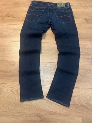 Mörkblå jeans Style 696 med raka ben - Snygga mörkblå jeans från Jacob Cohen, modell Style 696. Jeansen har raka ben, klassiska bakfickor och orangea detaljer vid dragkedjan. Tillverkade i mjukt denimtyg för en bekväm känsla och stilren look.