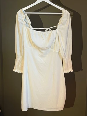 Vit kort klänning med snörning - Supersöt vit kort klänning med puffärmar och smock vid ärmsluten. Klänningen har en öppen rygg med snygg snörning och volangkant vid urringningen. Perfekt för sommarens alla tillfällen och ger en romantisk vibe. Passar helt perfekt till studenten! Köpt på BikBok och har aldrig använts, lappen sitter kvar 🤍🤍