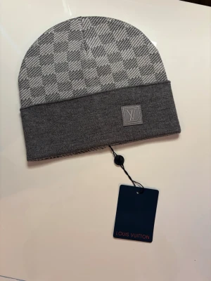 Grå rutig mössa  - Snygg grå mössa med klassiskt rutigt mönster och vikt kant. Diskret och exklusiv känsla. Perfekt accessoar för dig som vill ha något stilrent och lyxigt till vintern.