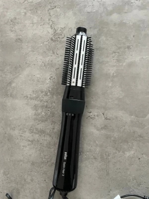 Svart varmluftsborste Braun Satin Hair 3 - En svart varmluftsborste från Braun Satin Hair 3 med rund borste och borstpiggar i plast. Handtaget har reglage för olika värmelägen och borsten har metallcylinder för jämn värmefördelning. Perfekt för styling och volym till håret.