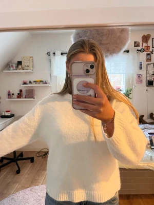 Vit stickad tröja med rund hals - Mysig vit stickad tröja med rund hals och långa ärmar. Tröjan har en avslappnad passform och ribbstickade muddar vid ärmslut och nederkant. Perfekt att matcha med jeans för en enkel och stilren look.