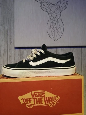 Svarta Vans Old Skool sneakers - Klassiska Vans Old Skool sneakers i svart med vit sula och vit sidostrip. Skorna har snörning och är tillverkade i mocka och canvas för en skön och stilren look. Perfekta för dig som gillar streetstyle och vill ha en ikonisk sko i garderoben. Säljer då jag växt ur dom har bara haft dom till kalas o sånt använda kanske 6 gånger,priset är ej fast