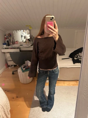 Brun långärmad topp med vid ärm - Säljer en brun långärmad topp med bred halsringning och vida ärmar. Toppen har en croppad passform och är tillverkad i ett mjukt material som känns skönt mot huden. Perfekt att styla med jeans eller kjol för en trendig look.