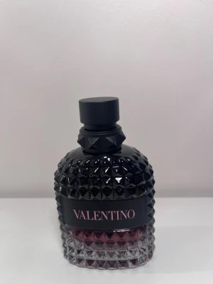 Valentino parfym med nitar - Snygg mansparfym från Valentino Born In Roma UOMO intense i en cool flaska med nitar och svart lock. Flaskan är svart upptill och övergår till transparent med en mörklila ton längst ner. Perfekt för dig som gillar lyxig design och vill ha något som sticker ut på hyllan. Endast använd få gånger och luktar otroligt.