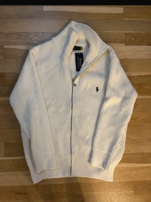 Vit ziptröja från Polo Ralph Lauren - En superunik tröja! Aldrig använd, i nyskick. Tröjan är tjock, varm och perfekt för vintern och höst/vår, både för en fin och bekväm look. Tröjan är för män. Säljer den pägrund av storleken. Den är i storlek M. Modellen på bild 2 är 178cm/72kg. Hör gärna av dig om du har några frågor eller funderingar!
