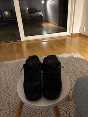 Svarta Nike Air Jordan 6 sneakers - Säljer ett par svarta Nike Air Jordan 7 sneakers med röda detaljer och klassisk snörning. Skorna har en låg siluett och är tillverkade i skinn och syntetmaterial. Perfekta för dig som vill ha en ikonisk och sportig look.