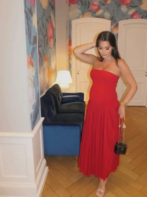 Röd axelbandslös långklänning - Trendig röd axelbandslös långklänning med figurnära överdel och vidd i kjolen. Klänningen har en enkel och stilren design som ger en elegant siluett. Ny med prislapp i storlek M ❤️