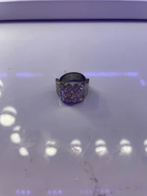 Silverfärgad ring med stenar - Cool silverfärgad ring från LOVYR med bred design och flera runda, glittrande stenar på ovansidan. Ringen har en unik form med vågig kant och ger ett statement-intryck. Perfekt för dig som gillar att sticka ut med accessoarer. Har haft den ett tag så den har rostat lite men knappt nåt som syns. Säljer på grund av att jag är en guld tjej så den kommer inte så mycket till användning. Men annars så tycker jag att den är jättefin. Justerbar men lite svår att ändra. Pris kan diskuteras.