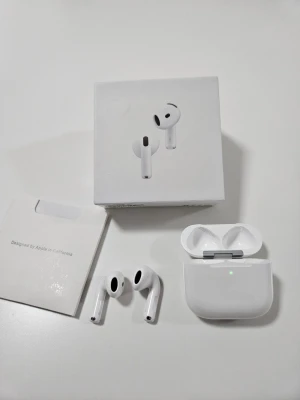 Apple AirPods trådlösa hörlurar - Snygga vita Apple AirPods med laddningsetui. De är trådlösa in-ear-hörlurar i stilren design med rundade kanter och diskreta svarta detaljer. Perfekta för musik, samtal och vardagsbruk. Kommer med originalförpackning och tillbehör.