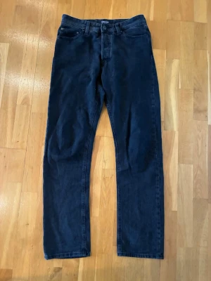 Svarta Relaxed/Chris jeans Jack & Jones - Snygga svarta jeans Jack&Jones i modellen Relaxed/Chris med klassisk femficksdesign och rak passform. Jeansen har en enkel look utan slitningar eller dekorationer, perfekta till en avslappnad stil. Tillverkade i mjukt jeansmaterial.