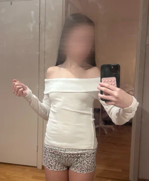 Vit offshoulder långärmad topp - Säljer en stilren vit offshoulder topp med långa ärmar. Toppen har en bred kant över axlarna som ger en snygg och modern look. Perfekt att matcha med jeans eller kjol för en trendig outfit.