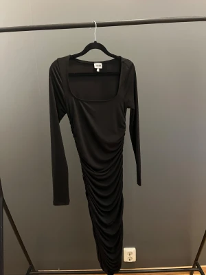 Svart långklänning med rynk - Säljer en svart långklänning från NA-KD med lång ärm och fyrkantig urringning. Klänningen formar sig väldigt fint efter kroppen & är ifrån Bubbleroom. Endast använd en gång så den är i mycket fint skick, storlek XS🖤