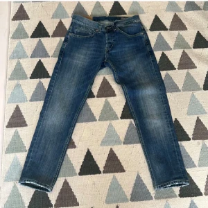 Blå dundop  jeans med orange detalj - Säljer ett par klassiska blå jeans från dondup med snyggt slitna detaljer och orange dundop-logga på bakfickan. Jeansen har raka ben, fyra fickor och kontrastsömmar på bakfickorna. Perfekta för en laidbak och cool Grisch stil 