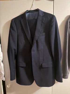 Mörkblå kostym och byxor - Snygg mörkblå kostym från Dressmann i slim fit-modell. Använd två gånger och ny kemtvättad.  Kavajen är i storlek 48 och byxorna storlek 34 - 32. Passade perfekt på mig som är 190