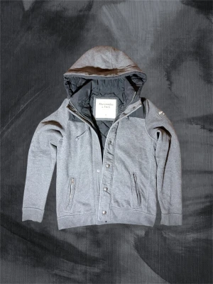 Grå quiltad jacka Abercrombie & Fitch - Tjena, säljer då denna sällsynta och mycket eftertraktad jacka/cardigan från Abercrombie. Med dubbla lager, luva i dun och mot kroppen är denna ett perfekt komplement till vinterhalvåret. Inga defekter, är som ny! Stilren och passar till allt, både i skolan och på hemmafronten. Missa inte chansen att slå till på denna! Tveka inte att höra av dig! 🤩 Modellen är 188 cm, väger 78 kg