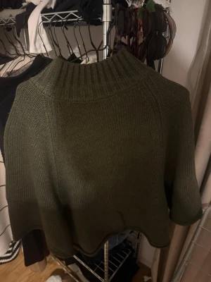 Olivgrön stickad polotröja från Zara - Snygg olivgrön stickad polotröja från Zara med bred ribbad krage och avslappnad passform. Tröjan har trekvartsärmar och är perfekt för lager-på-lager under hösten och vintern. Den grova stickningen ger en cool och mysig vibe.