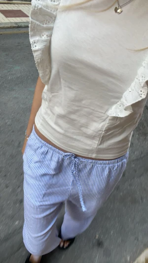 Vit blus med volangärmar - Supersöt vit blus med breda volangärmar i spetsdetaljer. Toppen är ärmlös och har en rund halsringning. Materialet känns som mjuk bomull och volangerna ger en romantisk vibe. Perfekt för varma dagar och att styla med smycken