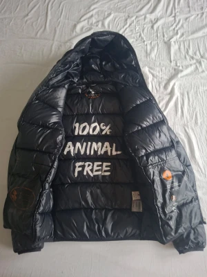 Svart pufferjacka från Save The Duck - Säljer en svart pufferjacka från Save The Duck med huva och dragkedja i storlek S. Jackan är lite sliten på texten på insidan (bild 3 och 4) förutom detta är jackan i mycket fint skick. 