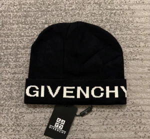 Svart mössa från Givenchy - Svart stickad mössa från Givenchy med vit logotyp broderad framtill på uppviket. Klassisk form och stilren design, fodrad med mjukt vitt tyg på insidan för extra komfort. Perfekt accessoar för att lyfta din streetwear-look.