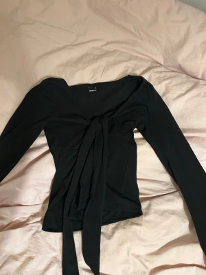 Svart  knyttopp från Gina Tricot🙏 - Säljer en svart långärmad topp från Gina Tricot med snygg knytning framtill. Toppen har något slim passform och är tillverkad i mjuk bomull. Perfekt för dig som gillar stilrena och trendiga plagg!🤩
