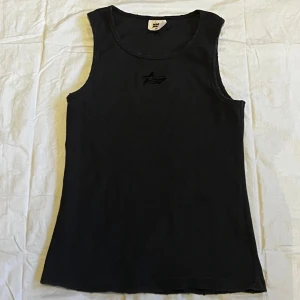 Svart ribbad linnetopp Broken Planet - Svart linnetopp från Broken Planet med ribbad struktur och broderad logga framtill. Modellen är ärmlös med rund halsringning och har en slim passform som sitter snyggt mot kroppen. Perfekt för dig som gillar stilrena och enkla plagg med cool detalj. Använd fåtal gånger