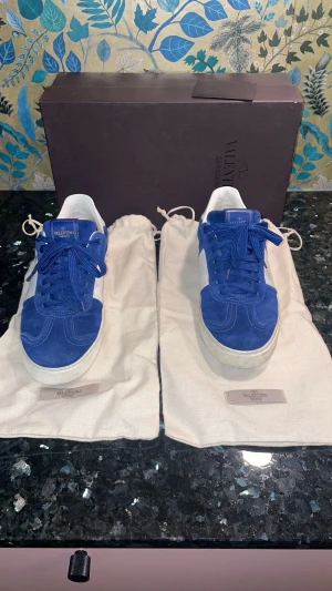 Valentino Garavani blå sneakers - Säljer ett par Valentino Garavani sneakers i blå mocka och vitt skinn. Skorna har snörning, rund tå och coola nitar på baksidan av sulan. Klassisk låg modell med vita detaljer och märkning på plösen. Kommer med originalpåse och box. Vid frågor skriv bara. 🤟🏽🤟🏽🤟🏽