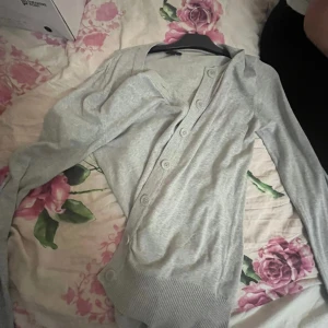 Ljusgrå kofta med knappar - Snygg ljusgrå kofta med långa ärmar och knappar framtill. Mjuk och tunn i bomullsmaterial, perfekt för lager-på-lager. Ribbad kant vid ärmslut och nederkant ger en clean look. Passar dig som gillar enkel och stilren vibe.